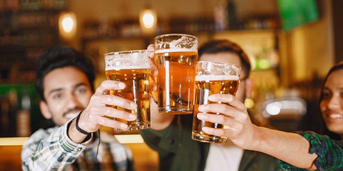 Indian friends in a pub. Guys and girl at  bar. Celebration over a mug of beer.